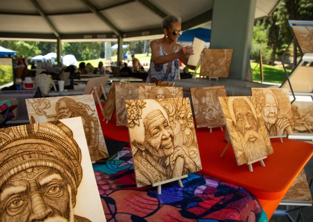 YaYa Comas, rear, sets up her laser-engraved artwork during the...