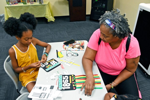 London McCraw, 12, of W. Baltimore, creates a banner as her grandmother, Christine Mitchell, of Washington Village, speaks with her about her creation. They are making unity bracelets, decorating flags and the banners during Juneteenth Crafts for Kids at the Cherry Hill Public Library on Tuesday. (Kim Hairston/Staff)