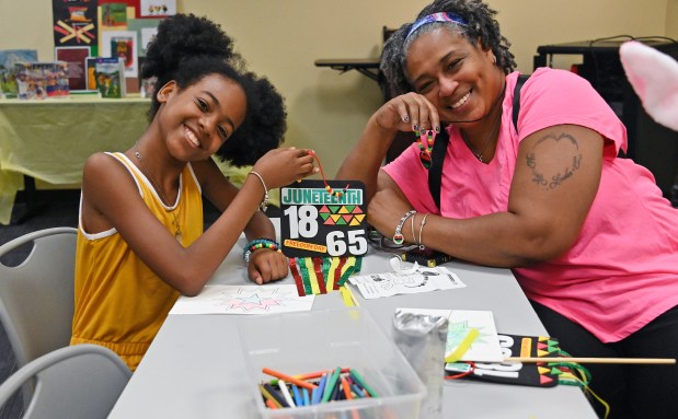 London McCraw, 12, of W. Baltimore, poses with her banner as her grandmother, Christine Mitchell, of Washington Village, pose with her necklace. They created the items at Juneteenth Crafts for Kids at the Cherry Hill Public Library on Tuesday. (Kim Hairston/Staff)